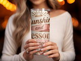 Tumbler with "Sunshine and Lessons" text and floral pattern held by a woman.