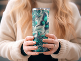 Woman holding a tumbler with a green and blue butterfly and swirling pattern.