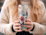Pink floral and butterfly design on a stainless steel tumbler held by hands.