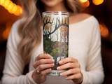 Woman holding a tumbler with a forest and deer hunting scene design.