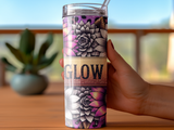 Tumbler with "GLOW" text and floral design held by a hand.