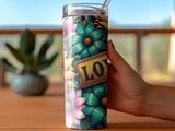 Tumbler with colorful floral design and "LOVE" sign held by hand.