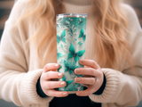 Tumbler with teal butterflies and glitter pattern held by person in cream sweater.