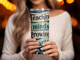 Woman holds a tumbler with "Teaching, Mends, Growing, Arts" text.