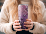 Purple tumbler with butterfly and floral design held by hands.