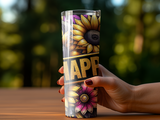 Hand holding a sunflower tumbler with "HAPPY" text against blurred green background.
