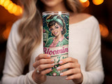 Woman holding a tumbler with "Bloom" and "Teacher Magic" text and a cartoon illustration.